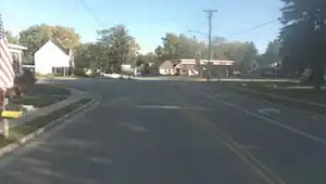 A street-level picture of a residential intersection, showing a sidewalk on the left with lowered curb ramp, and sidewalk on the right separated with a grassy verge.
