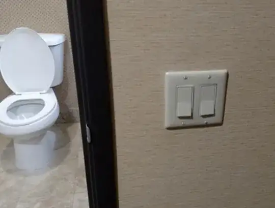 A light switch outside an opened bathroom door. Inside the bathroom is a toilet.