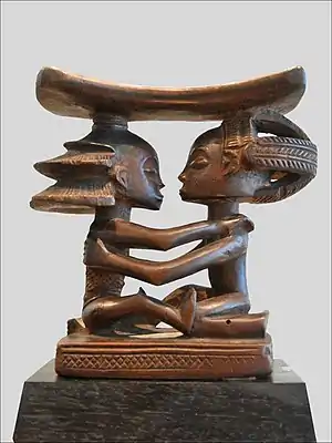 Headrest; 19th century; wood; height: 18.5&nbsp;cm (7.2&nbsp;in), width: 19&nbsp;cm (7.4&nbsp;in), thickness: 8&nbsp;cm (3.1&nbsp;in); Musée du quai Branly (Paris). This headrest presents 19th century Luba hairstyles, as well as the long limbs, bent-back legs, cylindrical torso and dynamic pose typical of the artist who made it