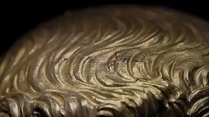 Small gray wave-shaped marks on a gold surface.