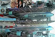 A metal-trussed hangar with a glass front and a shiny floor holds a large jet emblazoned with "United States of America" and other artifacts.