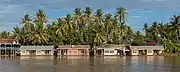 Colorful floating bungalows of Sala Don Khone Hotel, Mekong bank in front of tall palm trees, Don Khon in late afternoon, picture taken from Don Det.