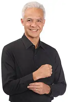 Official portrait of Ganjar Pranowo in 2023, showing him wearing a white ceremonial uniform displaying various medals. He is also wearing a black service cap with a Garuda Indonesia, the national symbol of Indonesia, on it. On the background is the Indonesian flag.