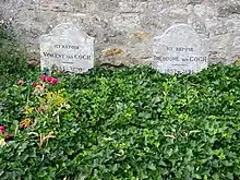 Two graves and two gravestones side by side; heading behind a bed of green leaves, bearing the remains of Vincent and Theo van Gogh, where they lie in the cemetery of Auvers-sur-Oise. The stone to the left bears the inscription: Ici Repose Vincent van Gogh (1853–1890) and the stone to the right reads: Ici Repose Theodore van Gogh (1857–1891)