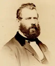 Sepia photo of Turcotte, half-profile head and shoulders;  dark hair and beard, wearing mid-Victorian business suit