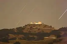 Time-lapse photograph of white buildings on top of a mountain at night with stars streaking across the sky.