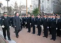 Macri, in an overcoat, walks down a line of young police officers