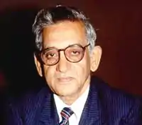 A photograph of an old man wearing blue suit and glasses.