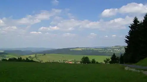 View from the Eckartsberg of Schnett and the Simmersberg (781&nbsp;m, right) with its subpeak, the Kohlberg (718&nbsp;m, centre). Between them in the background can be seen the Adlersberg (849,9&nbsp;m) with the Neuhäuser Hügel (891&nbsp;m). Left of the Kohlberg in the background is the trading estate of Suhl-Friedberg and the Little Thuringian Forest  with the Schleusinger Berg (671&nbsp;m) and Schneeberg (692&nbsp;m). Front centre is the village of Waffenrod/Hinterrod.