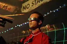 Professor Greg wearing a red uniform and wrap around visor.