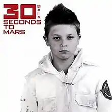 A boy with short hair. He wears a white jacket with a print on the left arm. In the top left, the words "30 Seconds to Mars" and four symbols are written in red font, with the "30" in bold.
