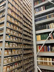 A tall metal shelving unit in a warehouse sized room, filled with bins holding books and other archive materials.